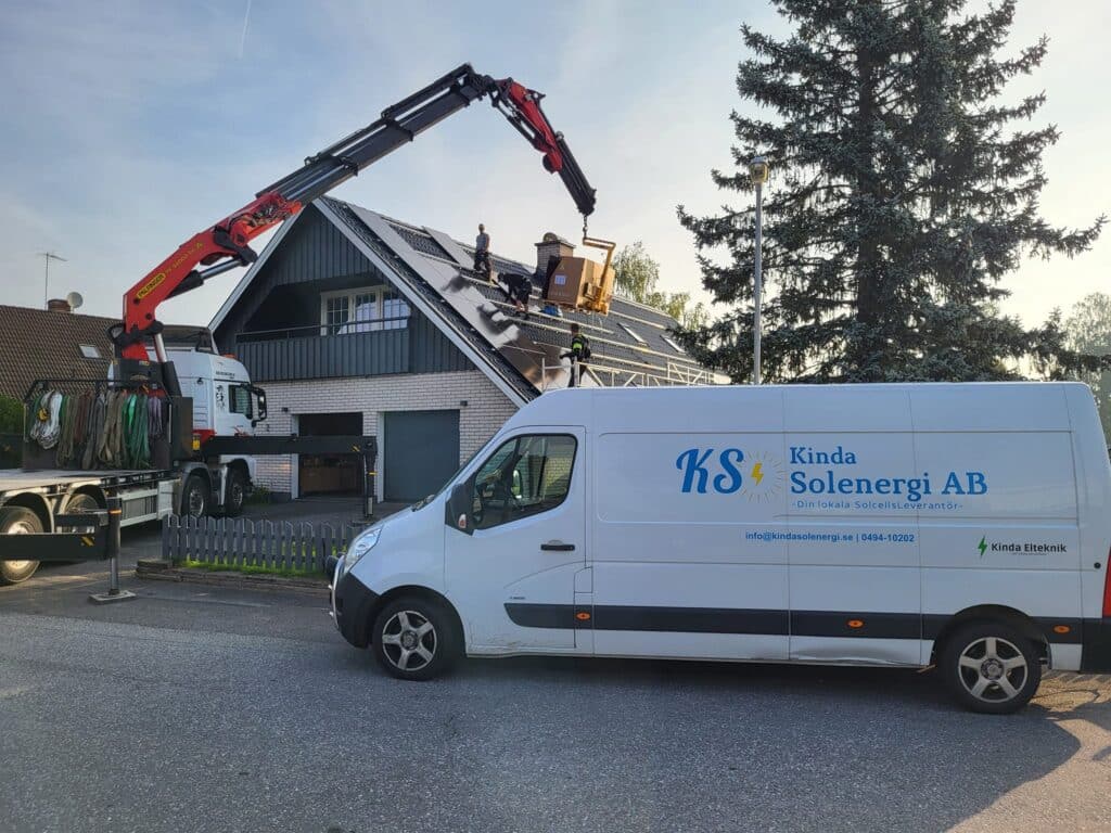 Kinda solenergis företagsbil parkerad framför ett hus med en lyftkran som håller på att installera solceller